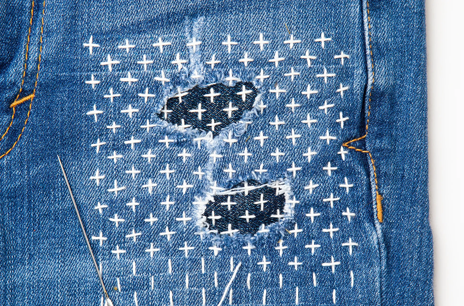 Sashiko visible mending on ripped denim jeans.