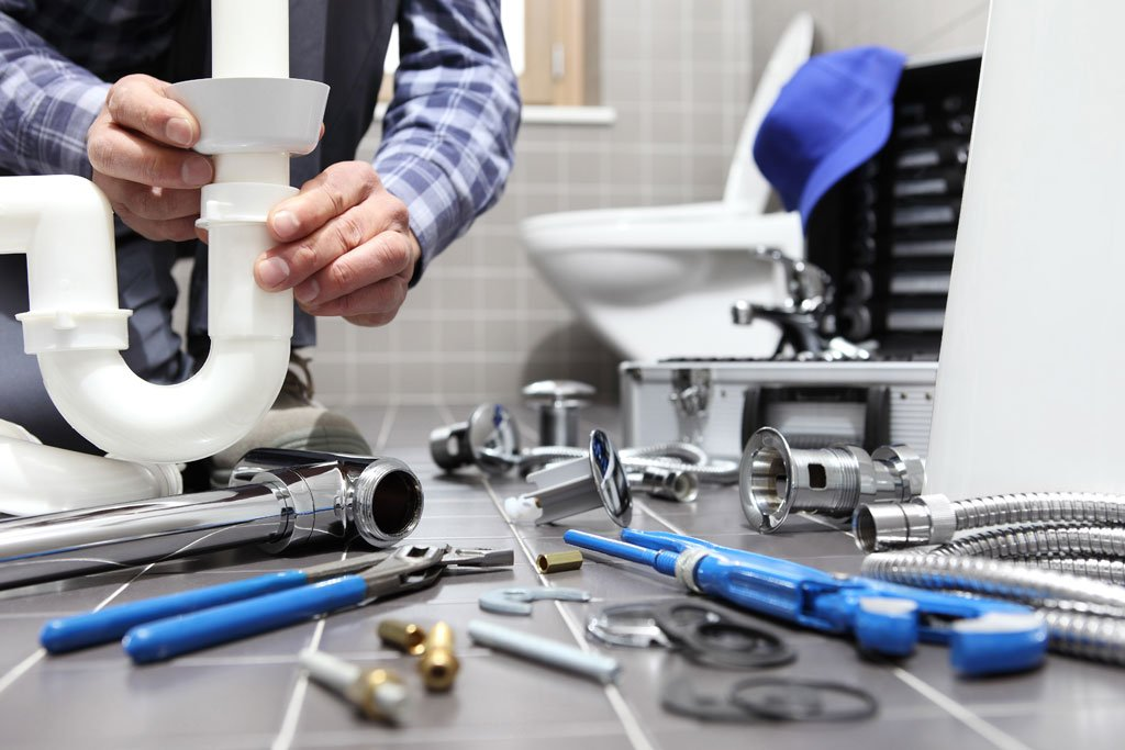 Plumber installing sink drain pipe using hand tools during bathroom plumbing repair
