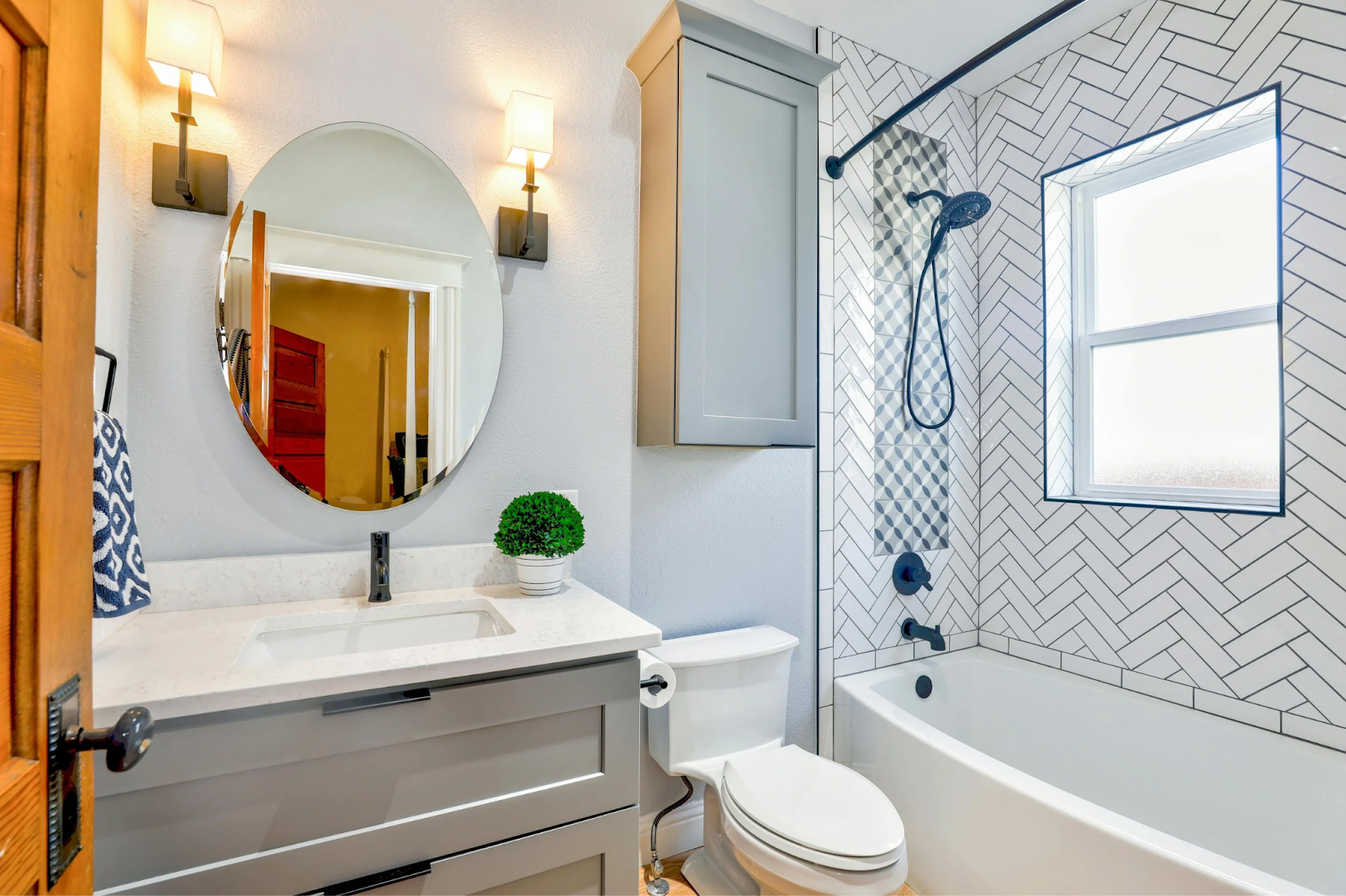 Modern bathroom vanity with round mirror, gray cabinets, and patterned tile shower wall