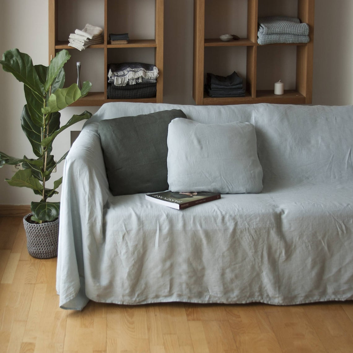 Minimalist living room with light gray sofa slipcover, wooden wall shelves, and indoor plant decor