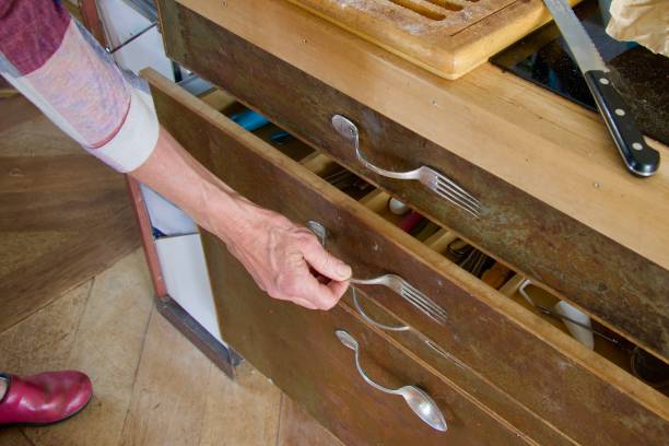A hand pulling the drawer of a kitchen cabinet made of upcycled forks and spoons