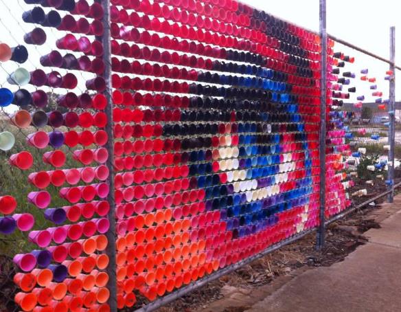 Cup mural art on chain-link fence forming an eye design