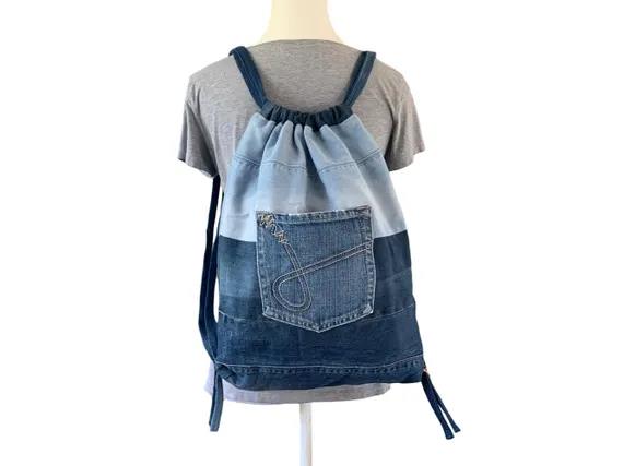 A handmade drawstring backpack constructed from recycled denim pieces, with a front pocket made from a jeans back pocket.