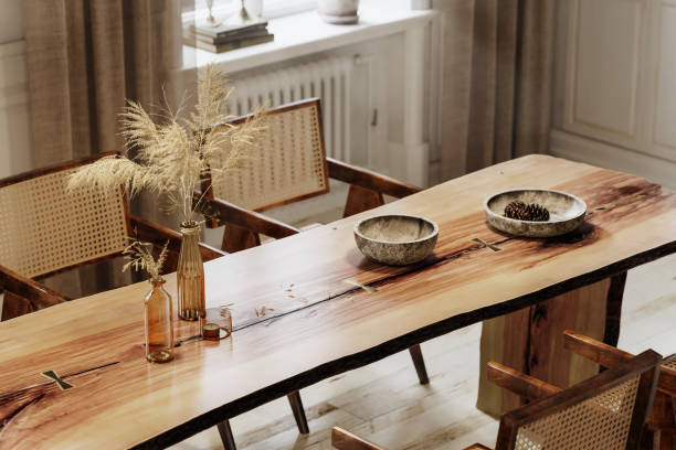 Rustic wooden dining table with natural edges, surrounded by wicker-back chairs and decorated with dried grass and ceramic bowls