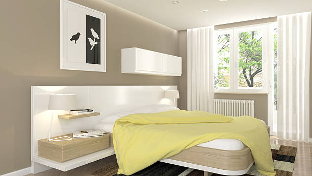A modern minimalist bedroom with a white platform bed, soft beige walls, large windows with sheer curtains, and a yellow blanket adding a pop of color.