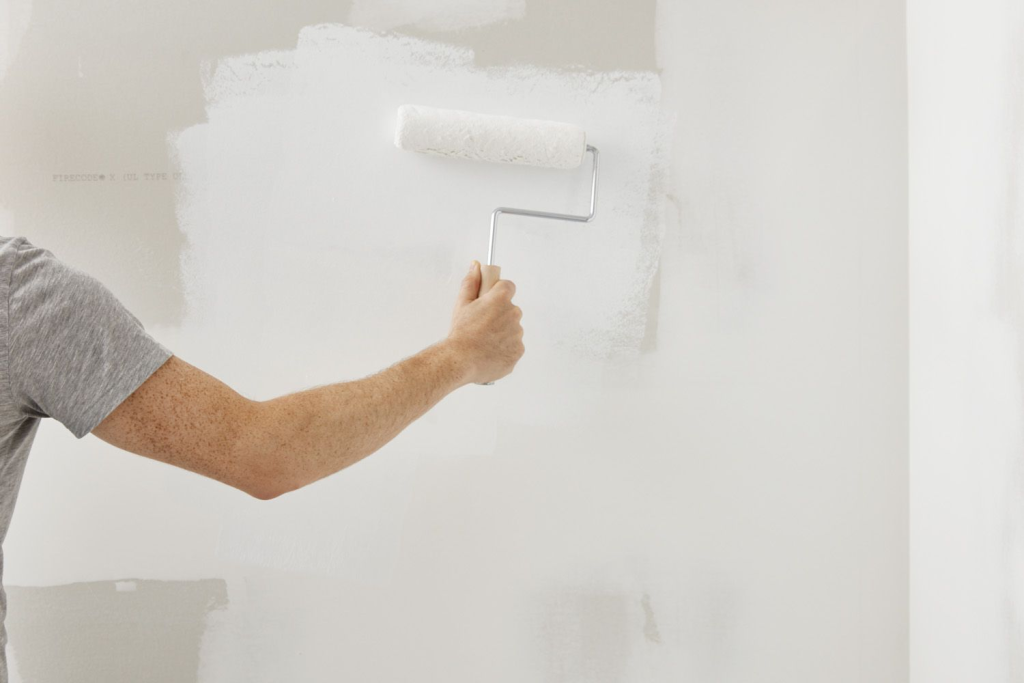 Individual applying primer using a paint roller on bare wall.