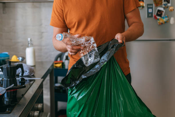 Young man holding green garbage bag and plastic bottle
