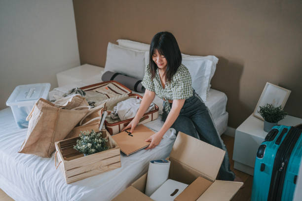 A woman sitting on the edge of a bed with boxes all around organizing the clutter.