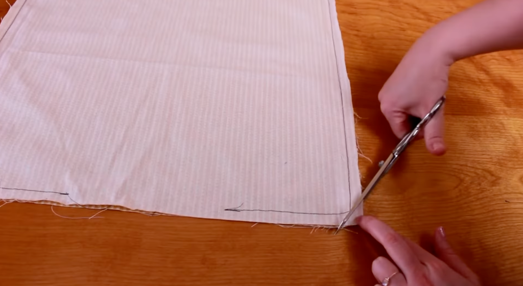 cutting fabric for DIY pillow cover sewing project with scissors on wooden table