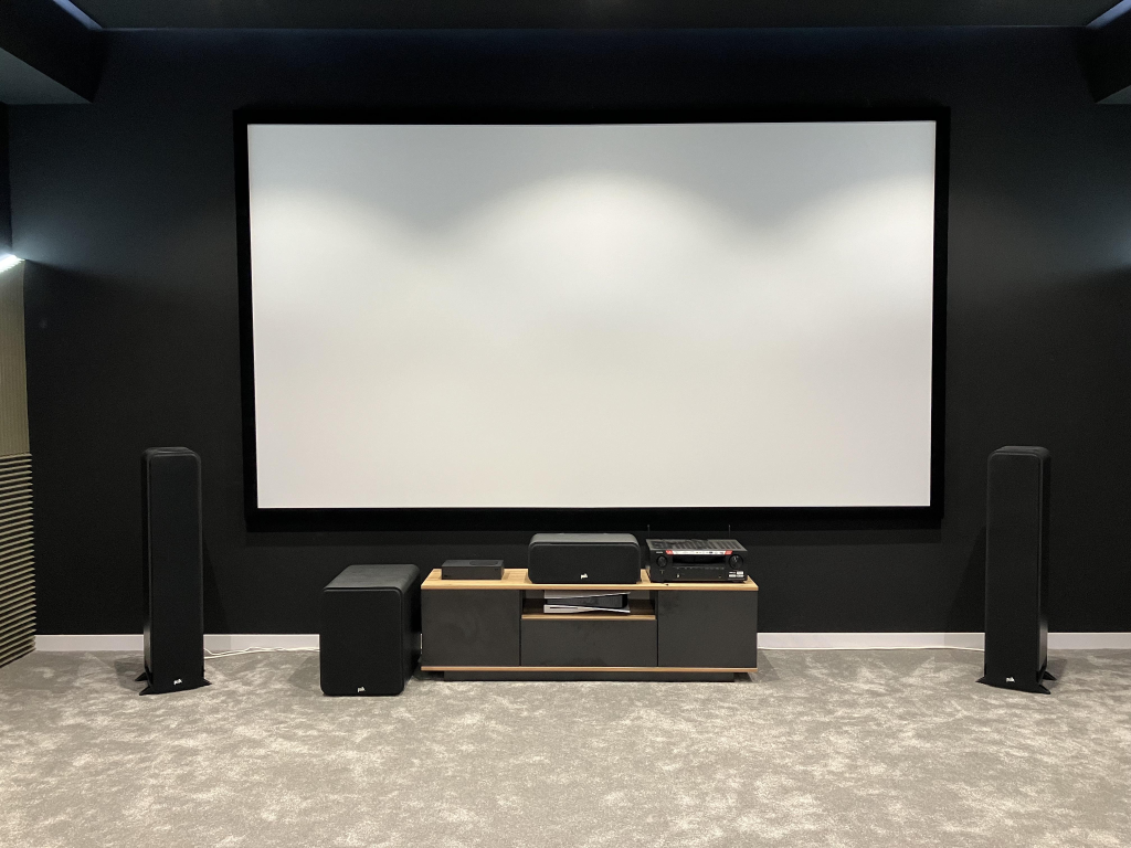 dark home cinema room with large projector screen surround sound speakers and carpet flooring