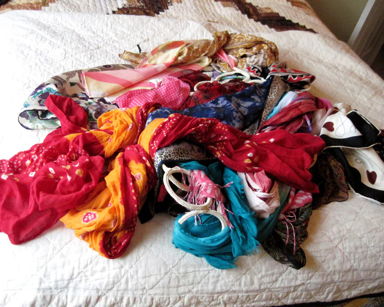 pile of mixed scarves on bed before organizing closet and decluttering wardrobe