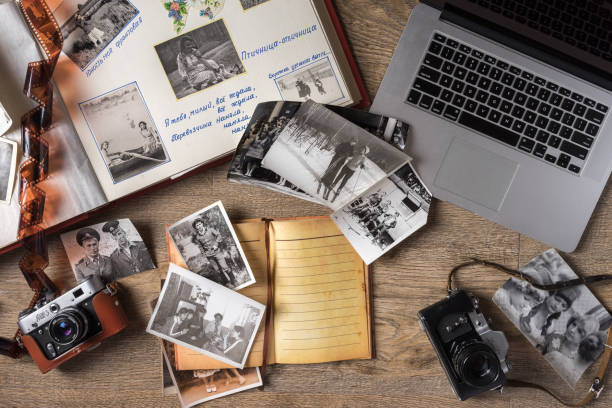 A top down view of black and white pictures, a laptop, a journal, a photo album, and two film cameras on a wooden floor.
