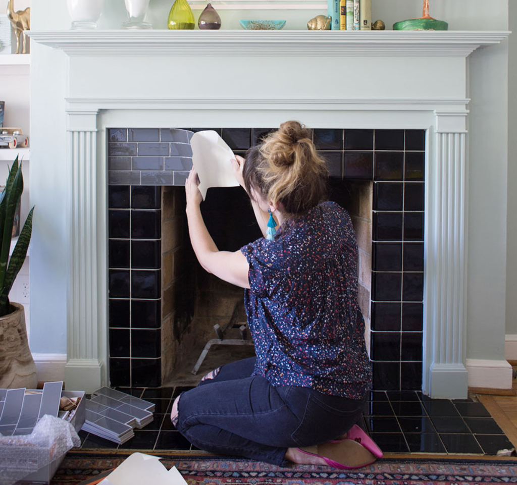 woman installing black subway tiles during DIY fireplace renovation project