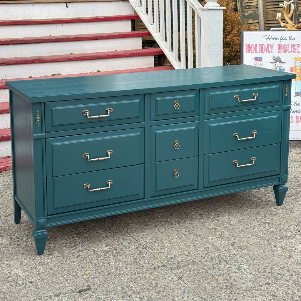 Teal lacquer dresser sitting outside at the bottom of a porch's stairs.