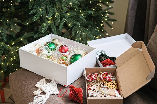 Organized Christmas ornaments stored in decorative boxes near decorated tree