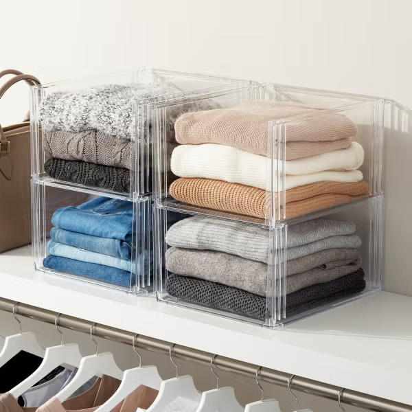 Sweaters stored in plastic organizers on the top shelf of a closet.
