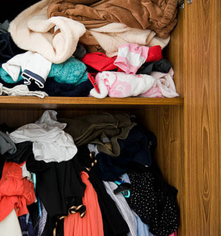A closet filled with clothing stuffed unorganized into compartments.
