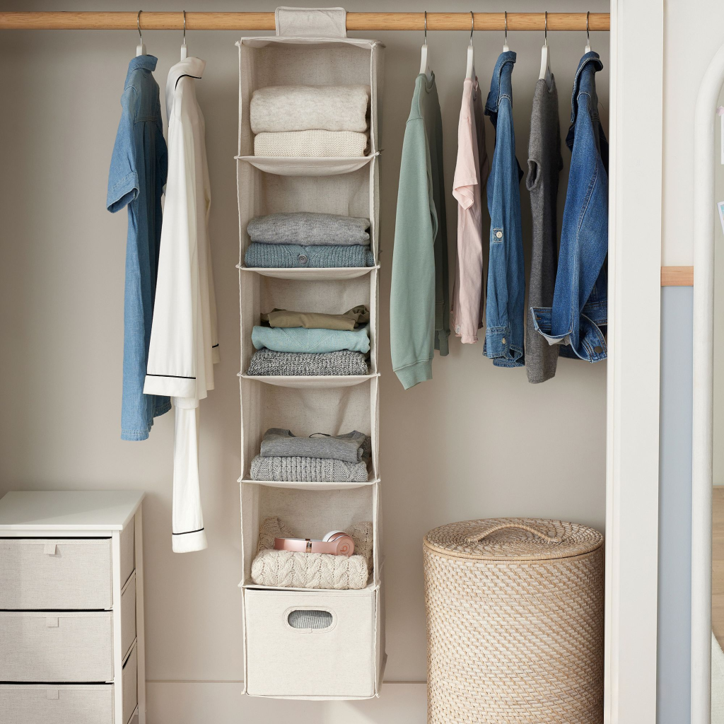 A hanging organizer with compartments that hold folded sweaters hung in a open closet.