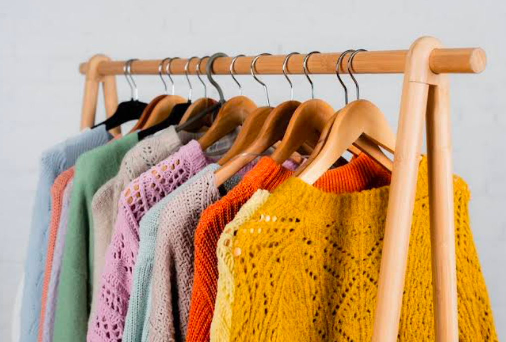 A standalone wooden rack with sweaters of varying colors hung up.