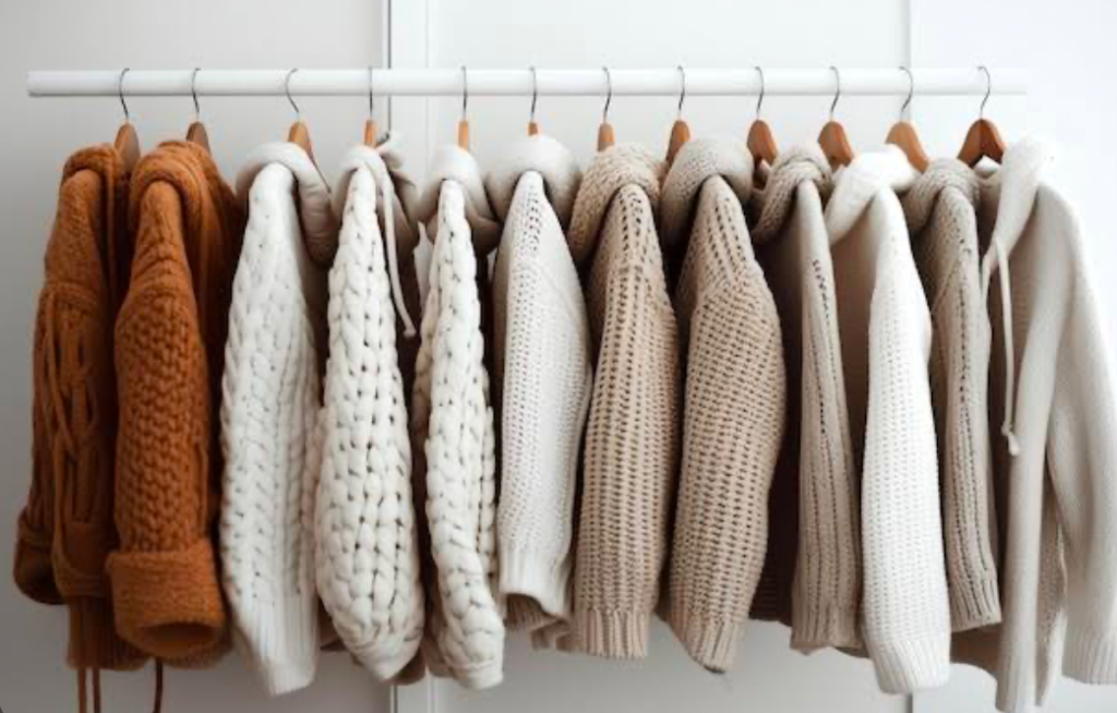 Sweaters organized by color in an open closet.