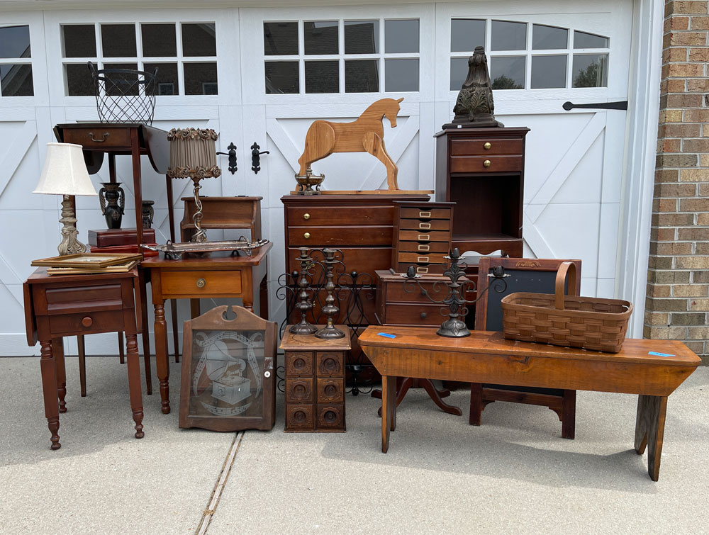A pile of furniture in front of a garage at a yard sale.