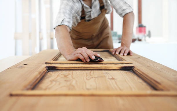person sanding wooden cabinet door before furniture refinishing and painting project