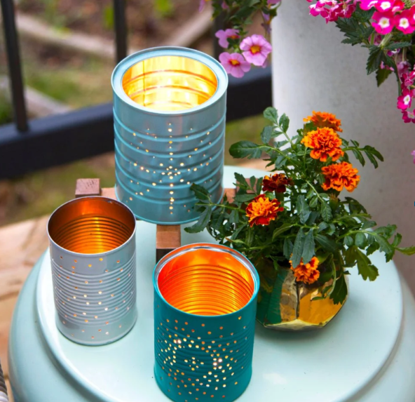 Three Tin can lanterns on a teal table next to a blossoming orange plant on the edge of a balcony.