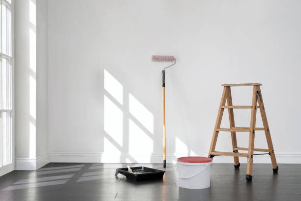 Painting supplies lined up against a white wall adjacent to a wall of windows.