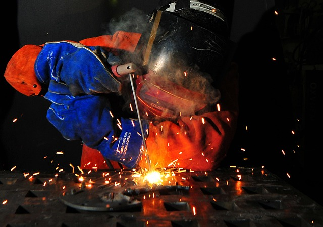 Welder working on a metal scrap in full protective gear.