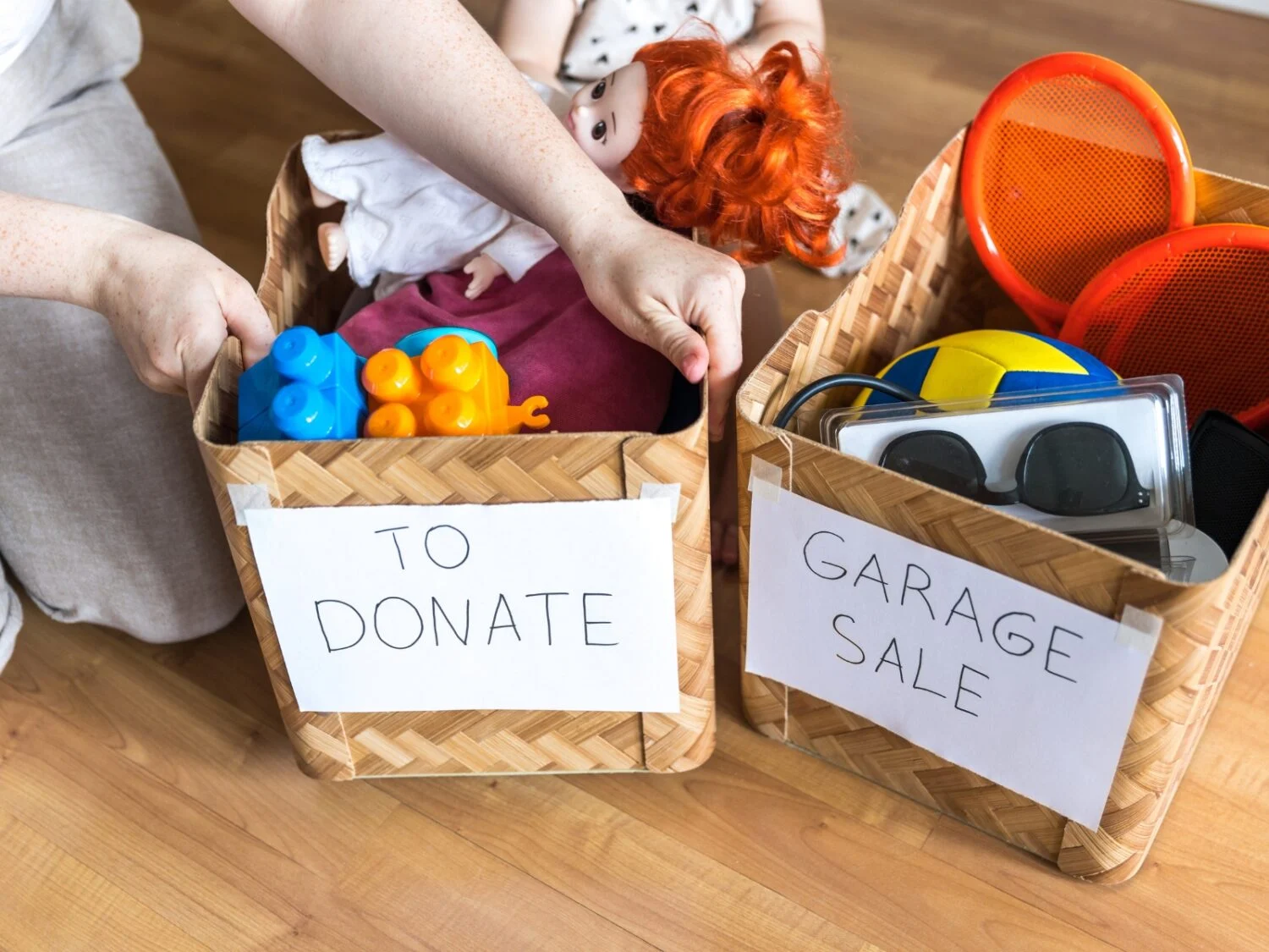 Two bins filled with toys, clothing, and other household items one labelled To Donate and the other bin labelled Garage Sale both resting on the floor.