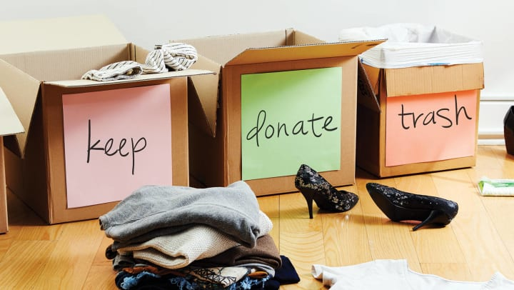 Three boxes on the floor labelled separately as Keep, donate, or trash with clothing and heels resting neat by.