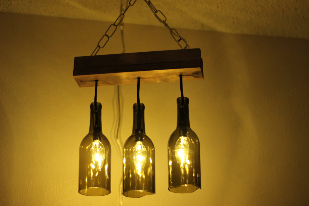 Repurposed wine bottles hung to a 2-by-4 holding three lights.