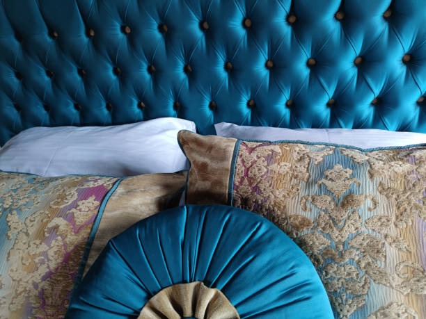 Luxury bedroom featuring teal tufted headboard and decorative silk pillows in gold and blue patterns