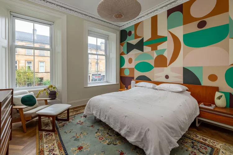 Abstract artwork as an accent wall in a bedroom next to windows filling the room with light.
