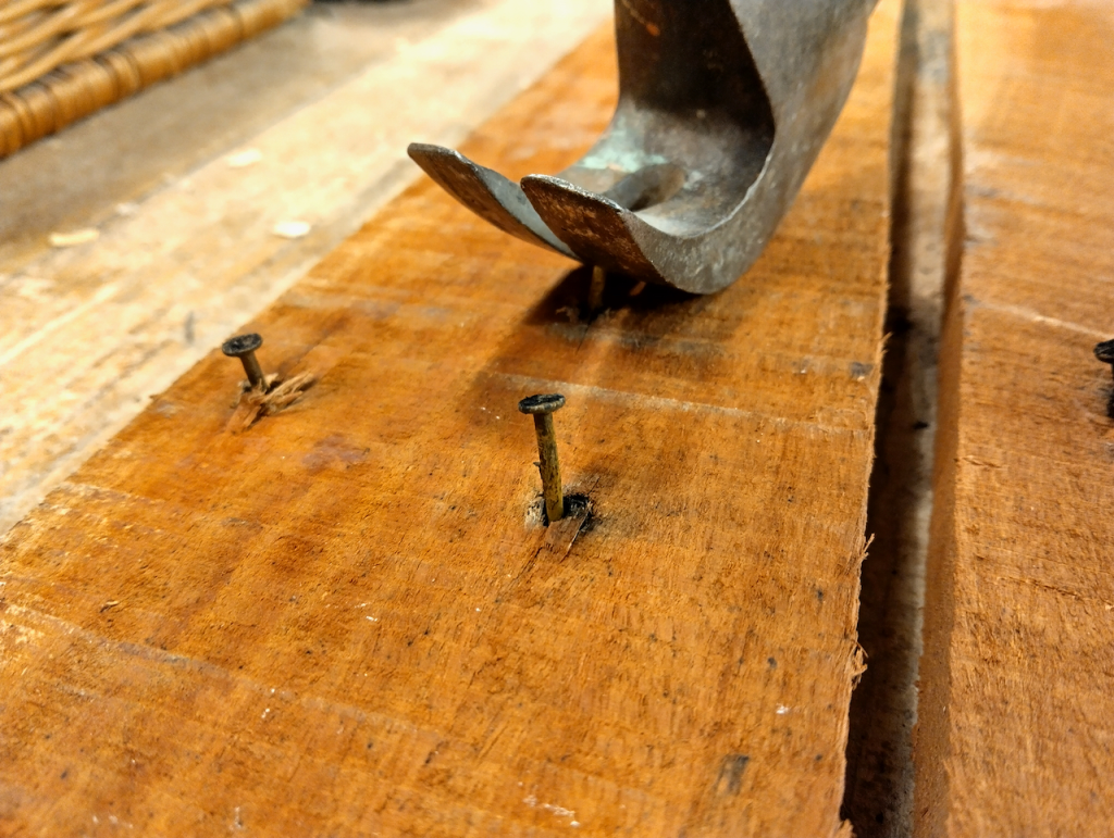 Close-up of crowbar removing rusty nails from pallet wood