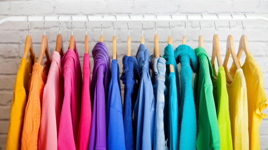Colorful sweaters organized on a rack in front of a white brick wall.