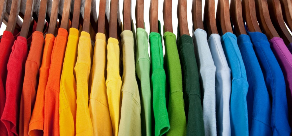 T-shirts arranged by color on wooden hangers.