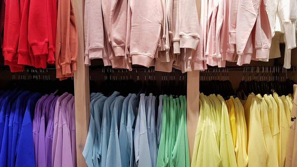 Closeup of a clothing store's upper and lower racks filled with colorful and organized long sleeved sweat shirts.