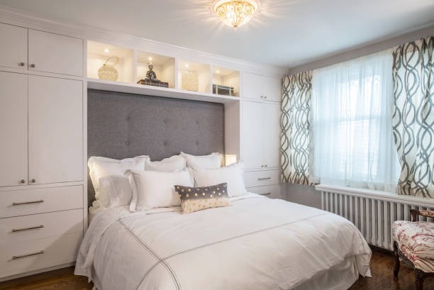 Small bedroom with built-in white storage cabinets, grey upholstered headboard, and layered white bedding