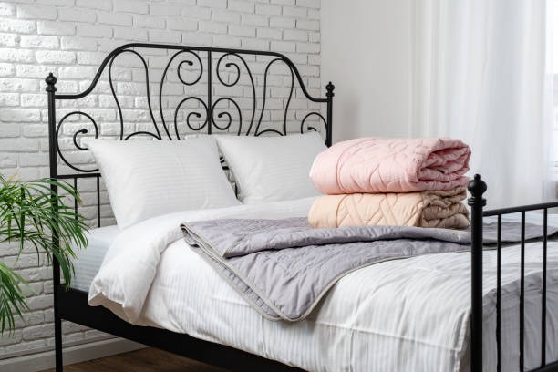 Cozy bedroom with black iron bed frame, white bedding, and folded pastel quilts stacked on top