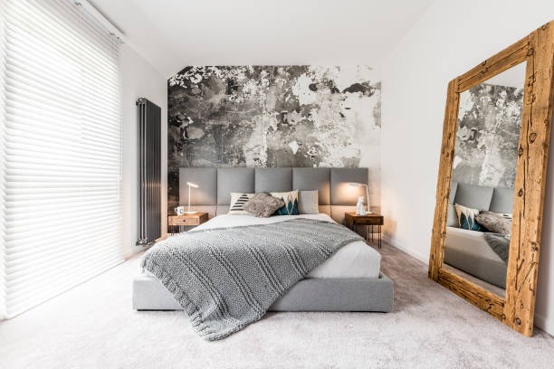 Contemporary bedroom with grey upholstered bed, textured feature wall, and large rustic wooden floor mirror