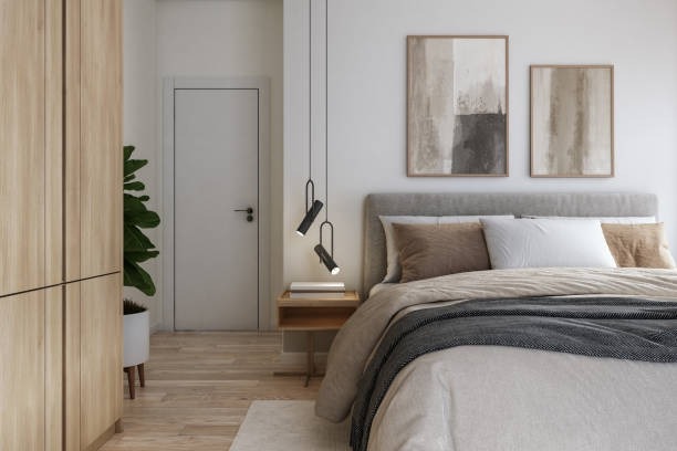 A neutral Scandinavian-style bedroom with a gray upholstered bed, minimalist pendant lights, beige bedding, wooden floors, and abstract artwork above the headboard.