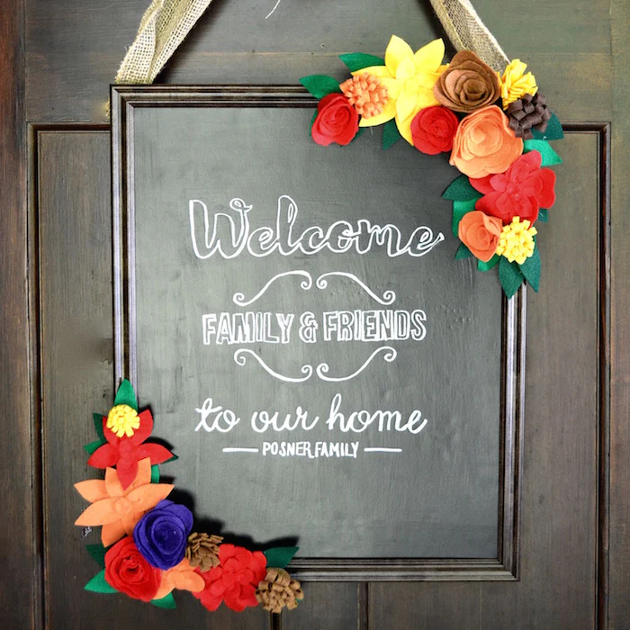 A chalkboard on a door giving a welcome message and both corners decorated with fall leaves.