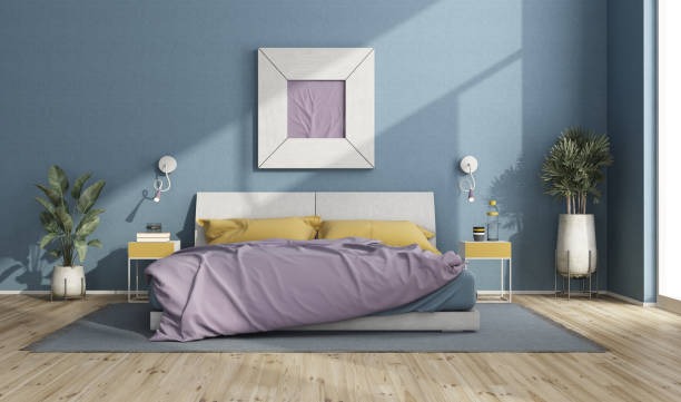 A serene modern bedroom with a blue feature wall, pastel bedding in lavender and yellow, symmetrical nightstands, and tall decorative plants on a wooden floor.