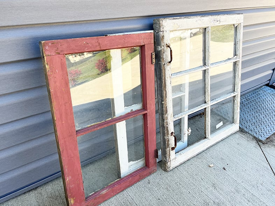 Two reclaimed window frames with chipped paint leaning against a house siding.