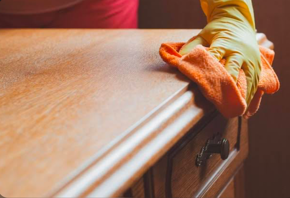 Hand wearing yellow glove cleaning a wooden cabinet with an orange cloth