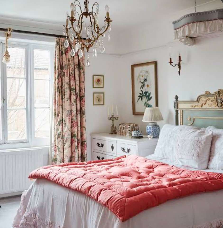 Cozy bedroom with floral curtains, a chandelier, and a coral comforter on the bed