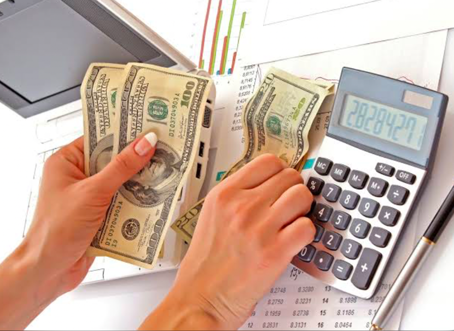 Hands counting US dollar bills beside a calculator and financial documents