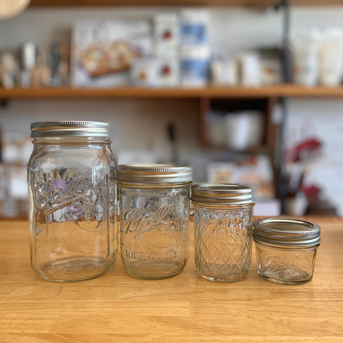 Old Mason Jars lined up from tallest to shortest on a table top.