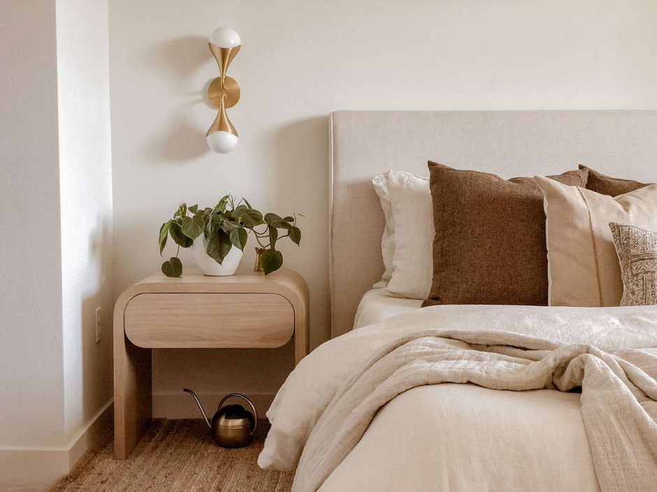 Minimalist bedroom with beige bedding, wooden nightstand, and indoor plant